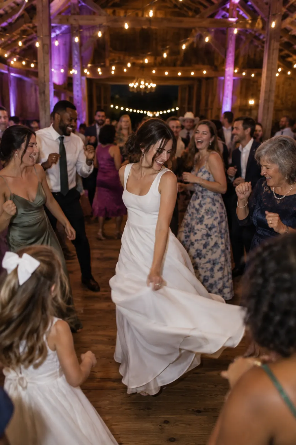 A bride dancing with her guests in a barn lit with string lights