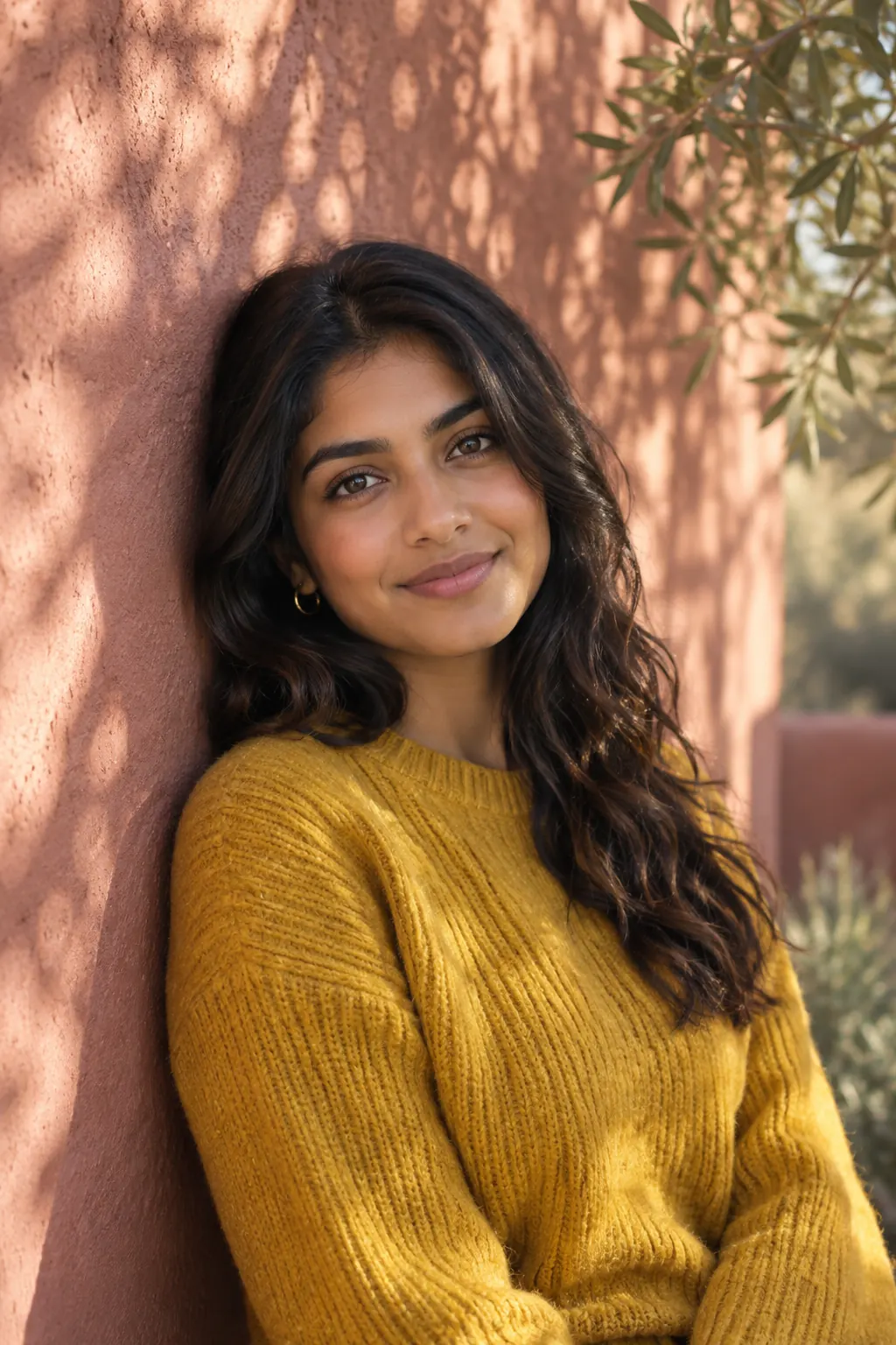 A young woman in a yellow sweater leaning on a pink adobe wall